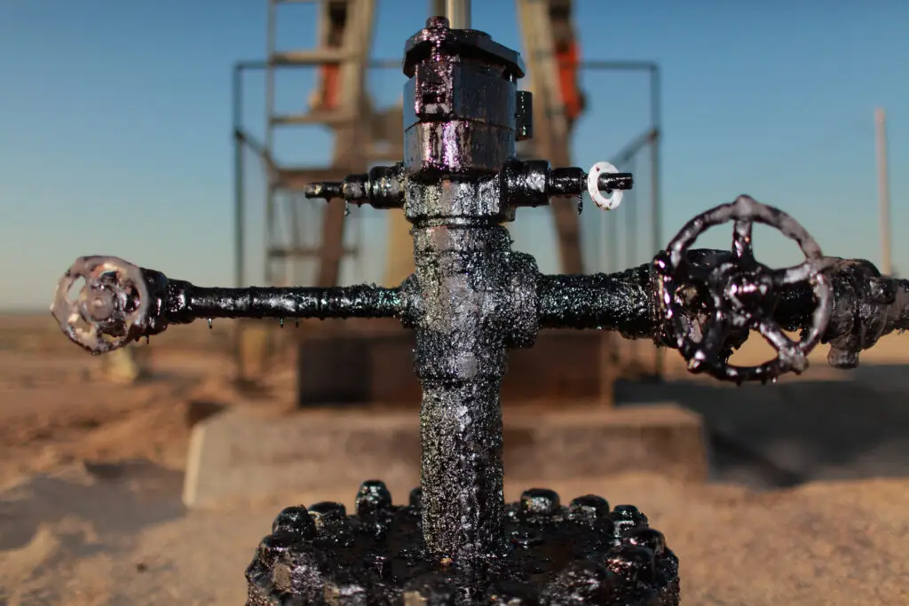 Close-up of an oil wellhead covered in crude oil residue at a drilling site.