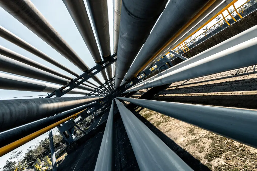 Industrial pipelines running parallel along a support structure at a refinery or processing facility.