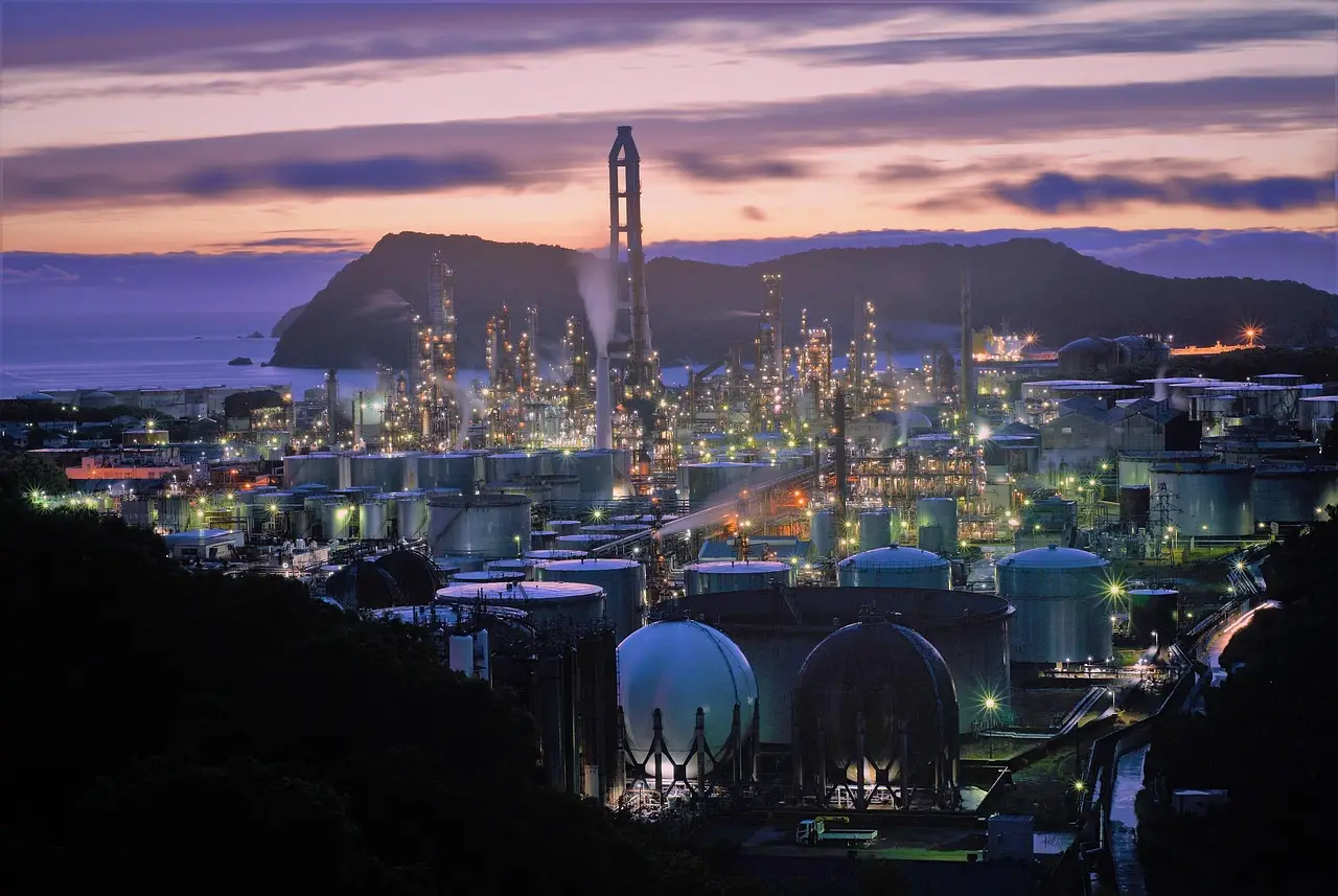 Large industrial refinery complex illuminated at dusk with storage tanks and processing towers near the Gulf Coast.